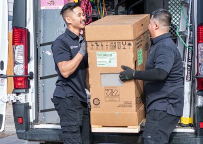 2 HVAC technicians unloading a box of equipment from the company van