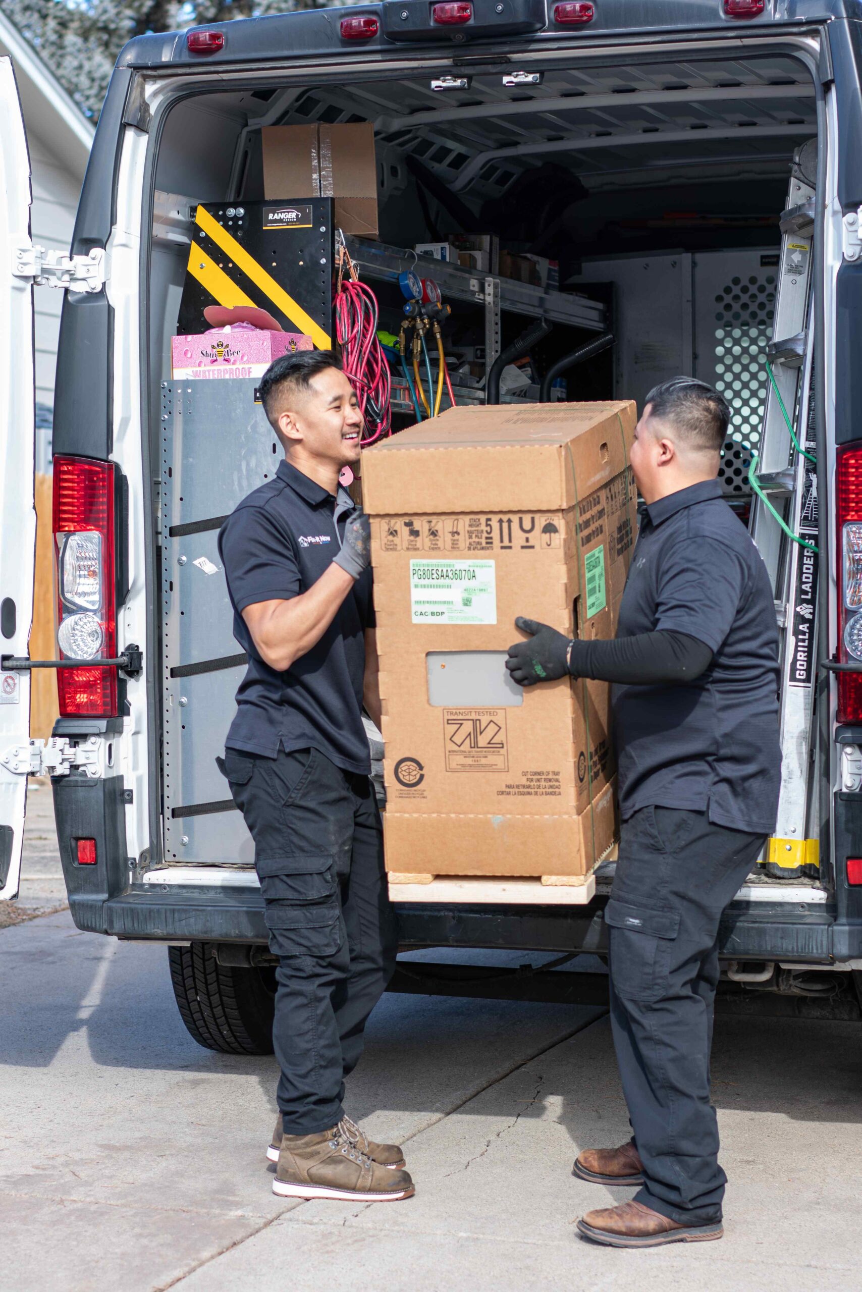 2 HVAC technicians unloading a box of equipment from the company van